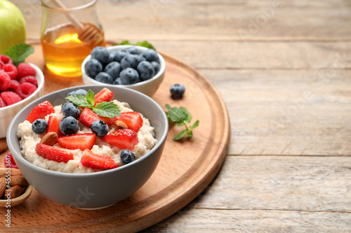 Tasty oatmeal porridge with berries and almond nuts served on wooden table, space for text