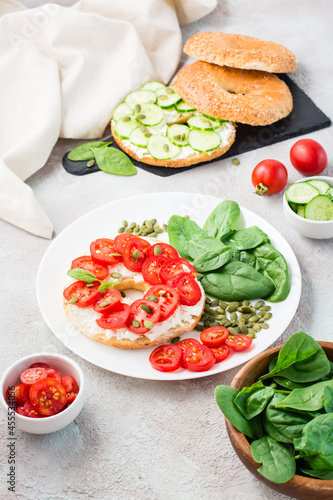 Delicious bagel stuffed with feta, tomatoes and pumpkin seeds and spinach leaves on a plate. Light Healthy Vitamin Snack. Vertical view
