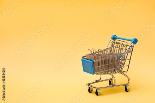 Eco-friendly shopping bags made of craft paper in a shopping cart on a yellow background. Black friday gift sales. Copy space