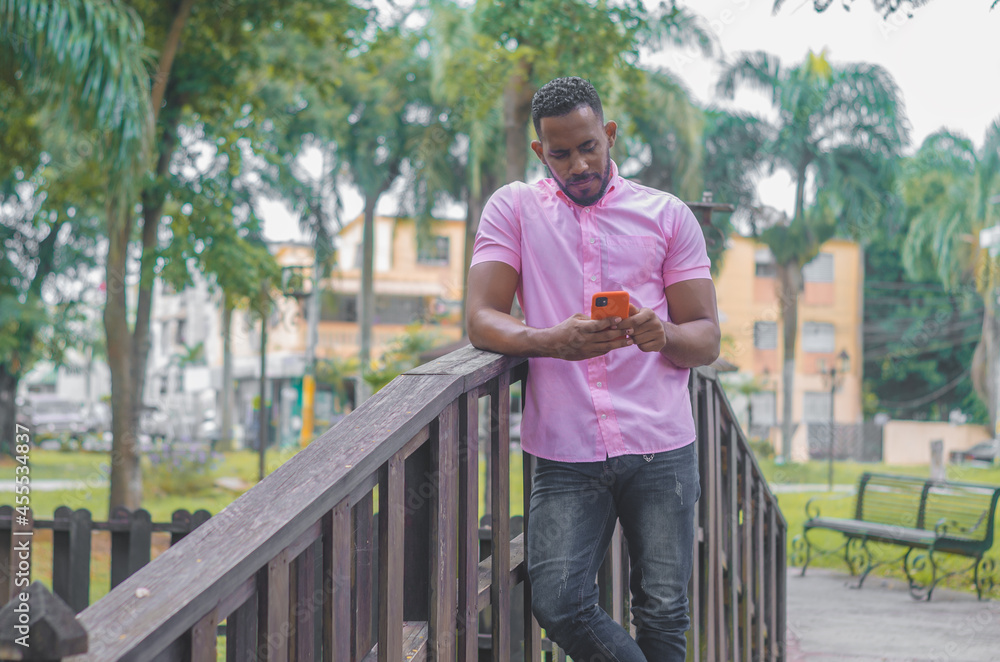 attractive dark-haired man of Dominican origin walking through the bridge having a call, talking on the phone, wearing a pink shirt attractive dark-haired man of Dominican origin walking through the bridge having a call, talking on the phone, wearing a pink shirt
