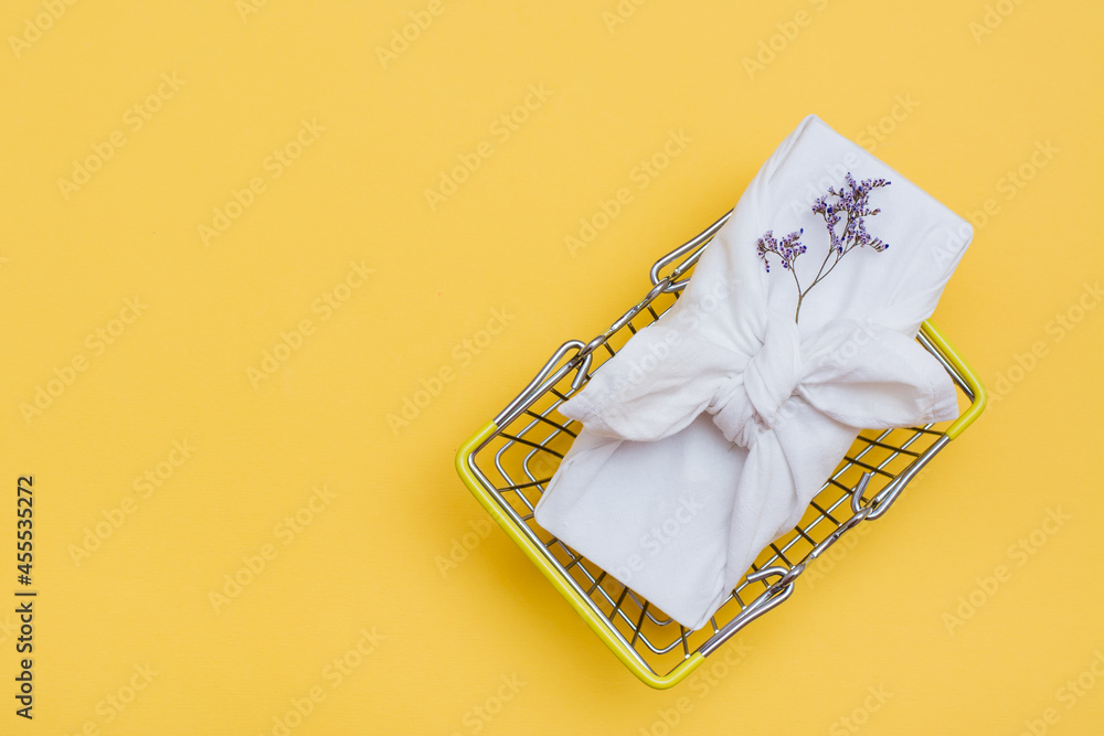 Eco-friendly furoshiki gift and dried flowers in a metal shopping basket on a yellow background. Black Friday, gift sales. Top view. Copy space Eco-friendly furoshiki gift and dried flowers in a metal shopping basket on a yellow background. Black Friday, gift sales. Top view. Copy space