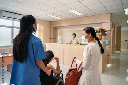 Nurse service pushing asian patient woman on wheelchair to contact the receptionist to admitted