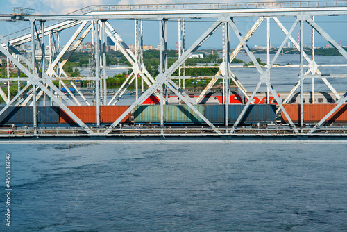 Railway train with colored containers moving along the bridge. © Vectorina