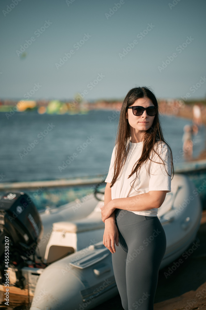 Young woman on the beach with long hair. Fit beautiful girl wears white shirt and gray leggings on the beach