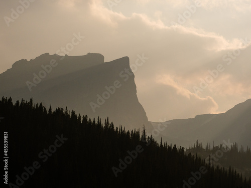 Landscape of forest silhouette and dramatic light shining on ridges of Rock Mountains. © Jessica