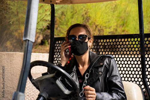 young woman with face mask in a golf buggy, talking on mobile phone
