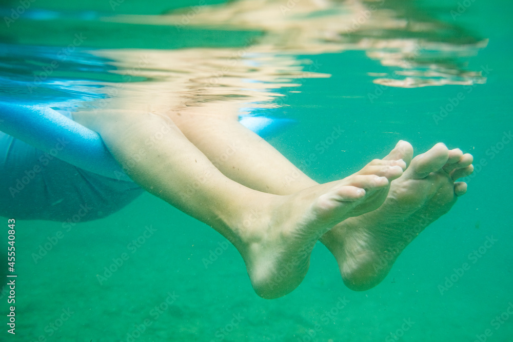 close up of woman's feet underwater flowing and floating while swimming in the sea with a flotation device known as pool noodle