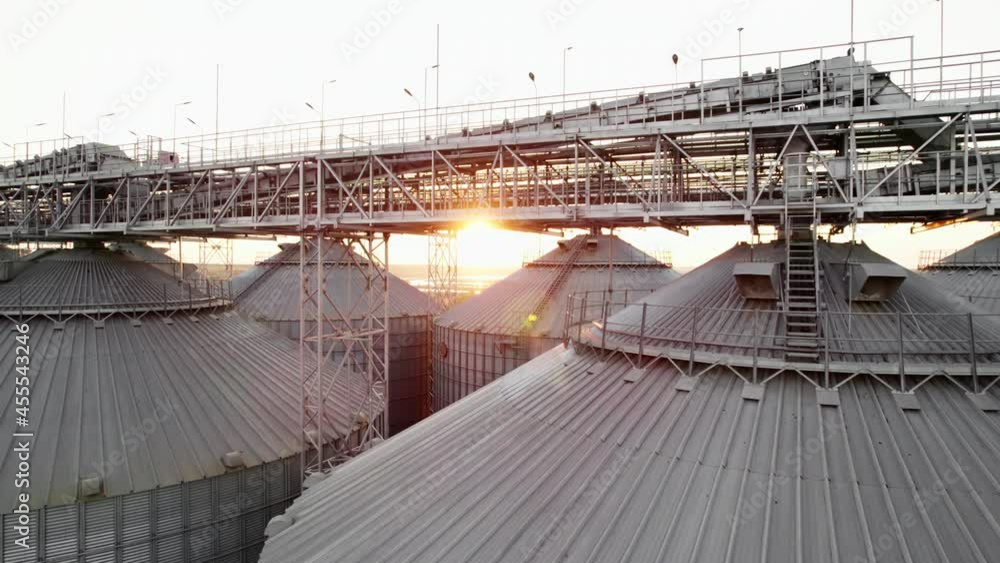 Farm Grain Storage Bins wheat field Aerial view at sunset from top. Steel Granary storage tanks steel warehouse granary for storage of loose grain lens flares on sea port Farm Grain Storage Bins wheat field Aerial view at sunset from top. Steel Granary storage tanks steel warehouse granary for storage of loose grain lens flares on sea port