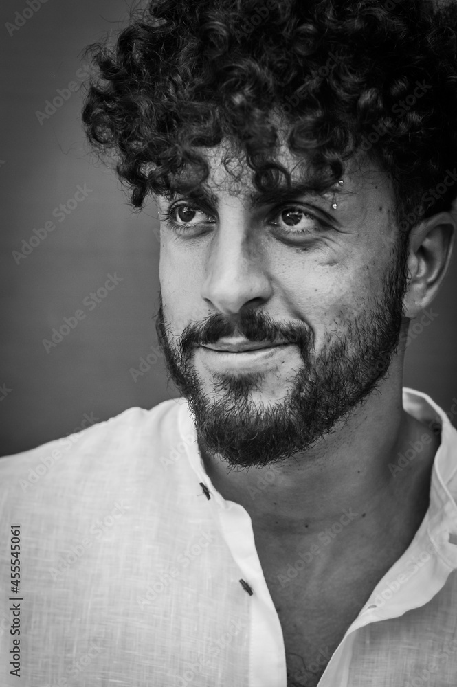 Fototapeta premium black and white portrait of a young man with beard and curly hair, who smiles slightly while looking away