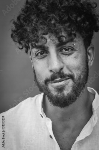 black and white portrait of a young man with beard and curly hair, who smiles slightly while looking at the camera