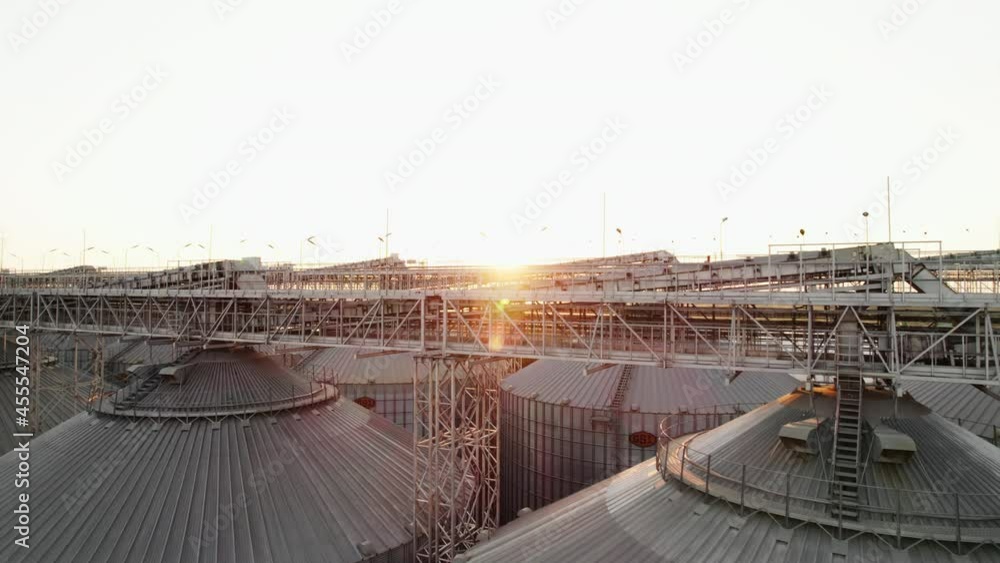 Aerial view Farm Grain Storage Bins wheat field at sunset from top. Steel Granary storage tanks steel warehouse granary for storage of loose grain lens flares on sea Aerial view Farm Grain Storage Bins wheat field at sunset from top. Steel Granary storage tanks steel warehouse granary for storage of loose grain lens flares on sea