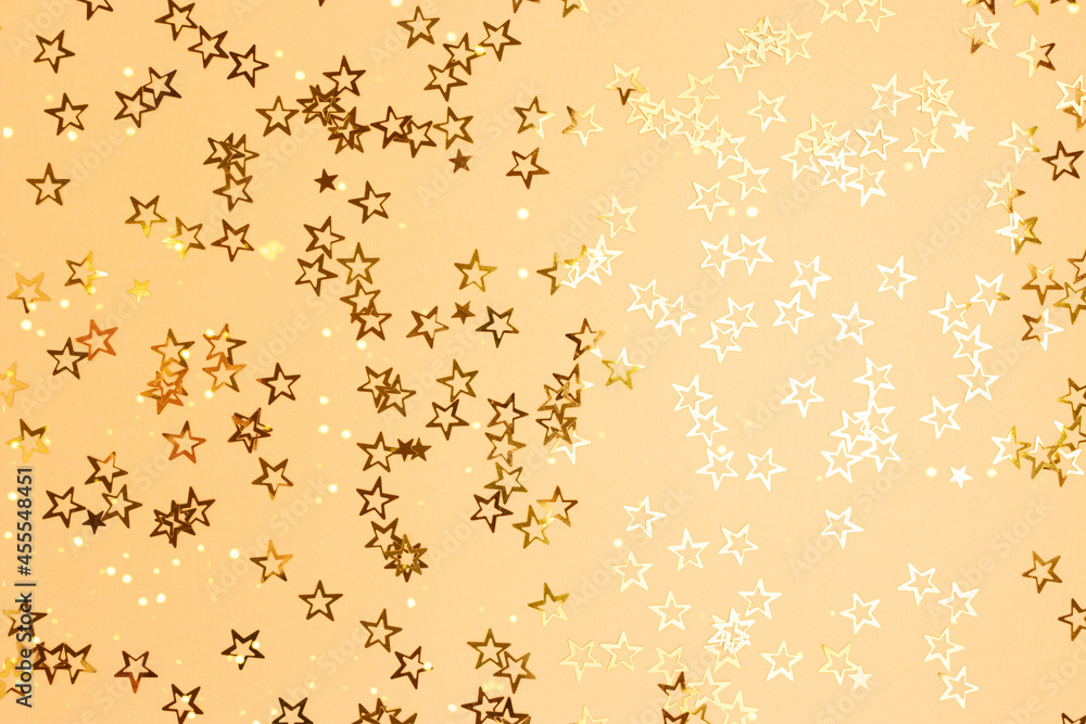 Monochrome composition with glittering stars confetti scattered on a gold background.