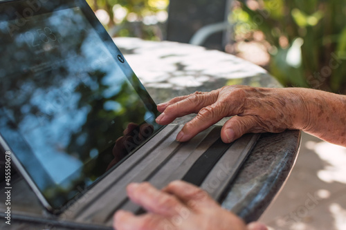 hands of elderly woman using a tablet outdoors on a sunny day, technology concept