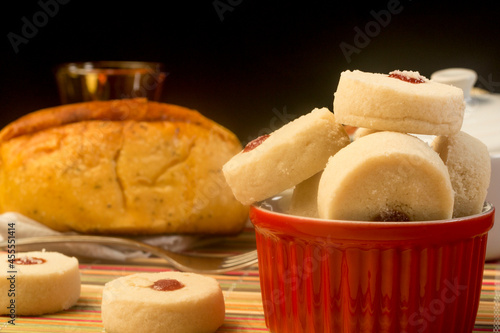 Biscoitos em tigela vermelha e pães ao fundo sobre uma mesa de madeira. Café da manhã completo. photo