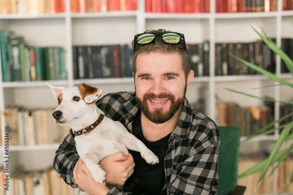 Φωτογραφία Happy male owner of jack russell terrier dog, feels responsibility of caring about pet, standing against bookshelves background