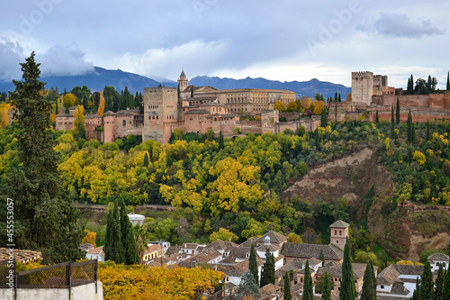 Landscape of the Alhambra on a cloudy day in autumn, the forest with green and yellow leaf trees and houses of the Albaicín