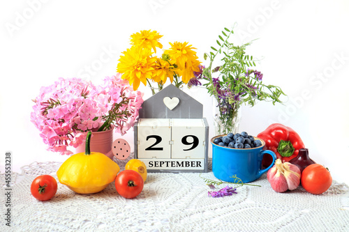 Calendar for September 29 : the name of the month in English, cubes with the number 29, ripe vegetables, bouquets of various flowers, blueberries in a blue cup on a gray napkin, white background photo