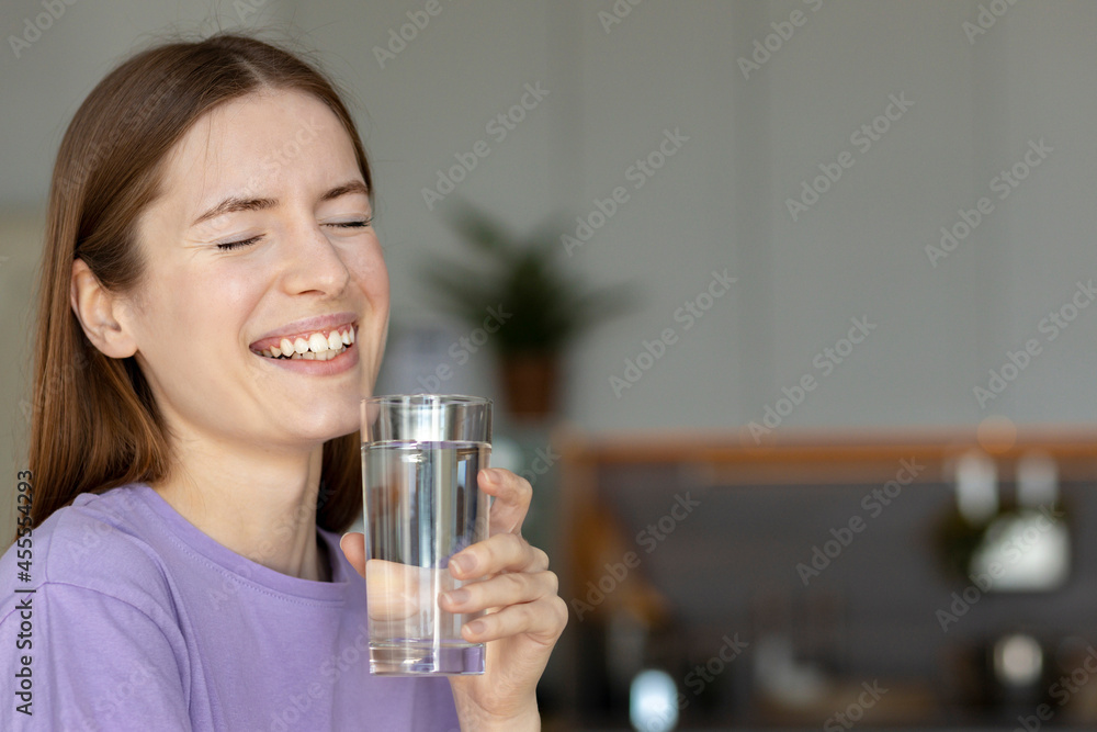 Smiling beautiful young woman drinking clear water  at home. Healthy lifestyle concept