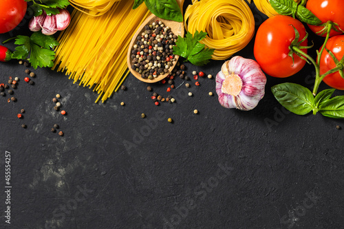 Italian food ingredients with pasta, tomatoes, pepper, garlic and parsley on dark background with copy space, top view