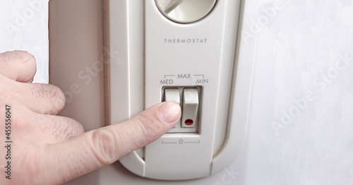 a man presses the button to switch the mode of operation of the electric oil heater.