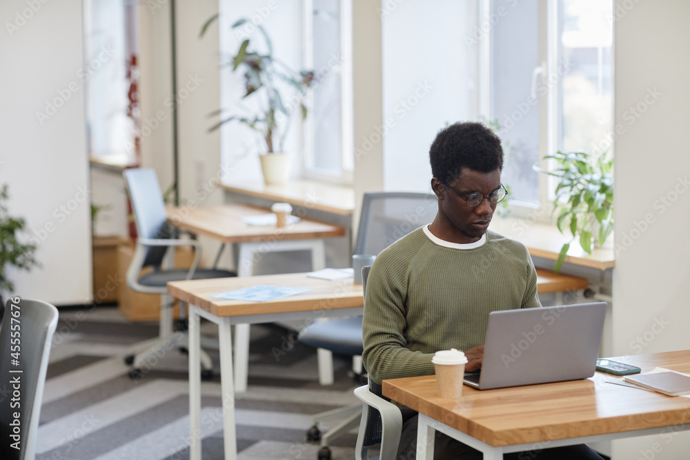 Frowning serious software developer drinking coffee and coding on laptop in open space office