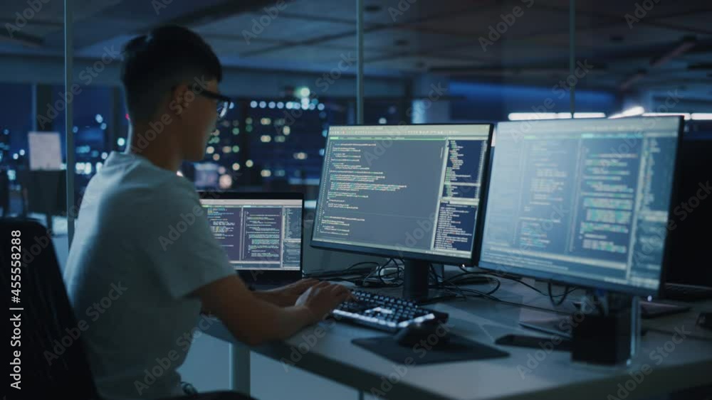 Night Office: Young Japanese Man in Working on Desktop Computer. Digital Entrepreneur Typing Code, Creating Modern Software, e-Commerce App Design, e-Business Programming. Over Shoulder Night Office: Young Japanese Man in Working on Desktop Computer. Digital Entrepreneur Typing Code, Creating Modern Software, e-Commerce App Design, e-Business Programming. Over Shoulder