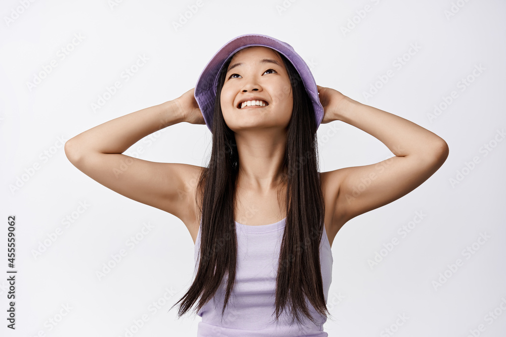 Image of happy asian girl on vacation, relaxing, holding hands behind head and looking up as if lying on beach, standing over white background Image of happy asian girl on vacation, relaxing, holding hands behind head and looking up as if lying on beach, standing over white background