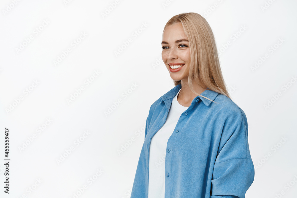 Portrait of young blond woman with white smile, looking aside with happy relaxed face expression, casual natural pose, standing over white background Portrait of young blond woman with white smile, looking aside with happy relaxed face expression, casual natural pose, standing over white background