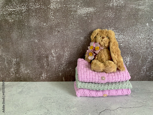 Cozy, warm pink and grey baby sweaters, knitted clothes on a table. Stack of handemade garment with a rabbit on top. Gray background with copy space and place for text. Childhood concept. photo