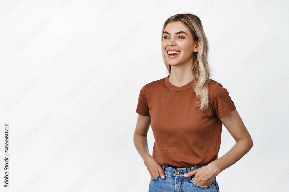 Obraz premium Young happy woman with blond hair, looking aside with friendly smile, talking to someone and laughing, standing against white background