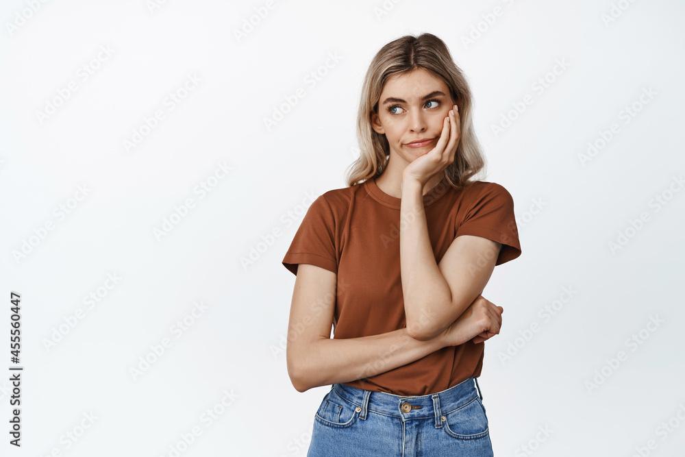 Thoughtful blond girl looking left with troubled face, thinking and pouting, standing in tshirt against white background Thoughtful blond girl looking left with troubled face, thinking and pouting, standing in tshirt against white background