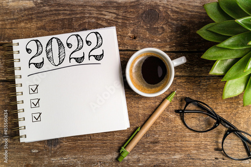 New year goals 2022 on desk. 2022 goals list with notebook, coffee cup, plant on wooden table. Resolutions, plan, goals, action, checklist, idea concept. New Year 2022 template, copy space