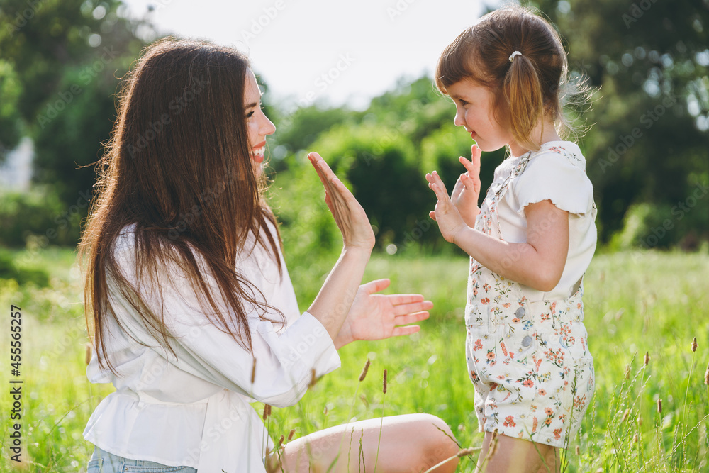 Happy smiling young woman in white clothes have fun with cute child baby girl 5-6 years old Mommy play clap your hands rest with little kid daughter outdoor together. Mother's Day love family concept Happy smiling young woman in white clothes have fun with cute child baby girl 5-6 years old Mommy play clap your hands rest with little kid daughter outdoor together. Mother's Day love family concept
