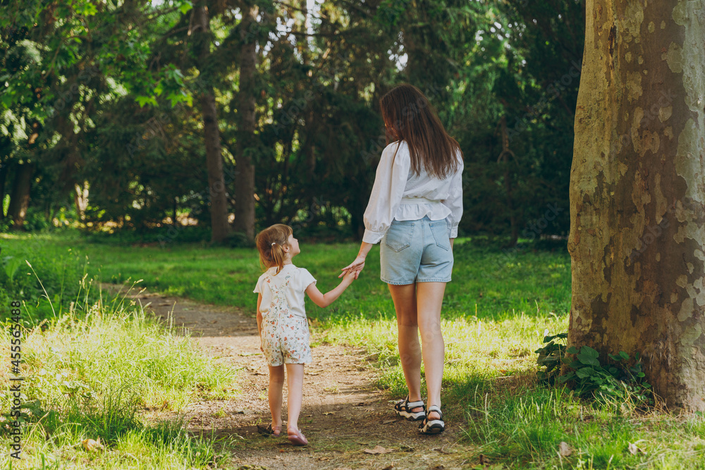 Full body back view young woman in white clothes have fun with cute child baby girl 5-6 year old walk along forest path Mommy play rest with little kid daughter outdoor together Love family concept Full body back view young woman in white clothes have fun with cute child baby girl 5-6 year old walk along forest path Mommy play rest with little kid daughter outdoor together Love family concept