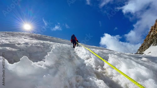 Two young women Rope team ascending Mont Blanc (Monte Bianco) summit 4,808m dressed mountaineering clothes with ice axes connected with bright rope. People extreme activities sporty concept image. photo