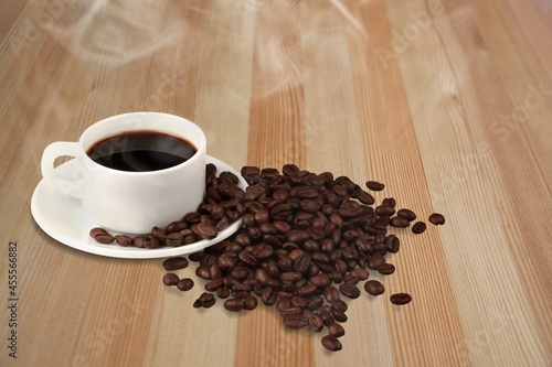A cup of coffee among selected coffee beans scattered on a table,