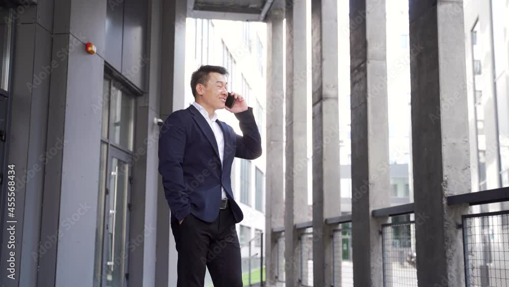 portrait successful young confident businessman talking background modern office building in downtown. Happy Asian business man conversation a mobile phone standing in formal suit outdoor, city street portrait successful young confident businessman talking background modern office building in downtown. Happy Asian business man conversation a mobile phone standing in formal suit outdoor, city street