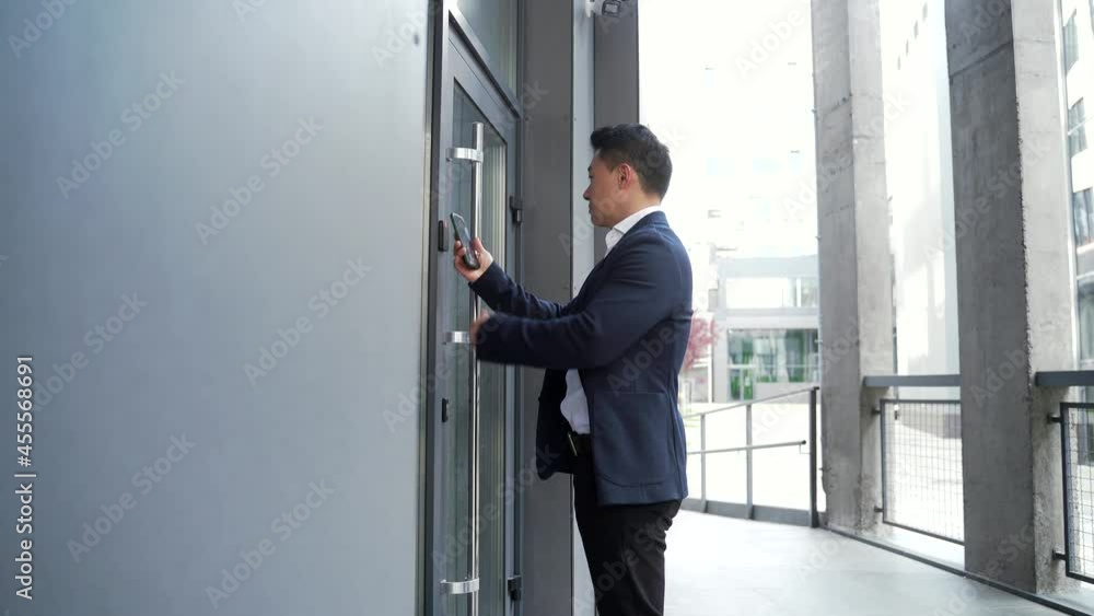 male asian businessman unlocking door using mobile phone application. Unlocks a modern office building. Scanning open smartphone with mock up screen app. smart electronic locks with keyless access male asian businessman unlocking door using mobile phone application. Unlocks a modern office building. Scanning open smartphone with mock up screen app. smart electronic locks with keyless access