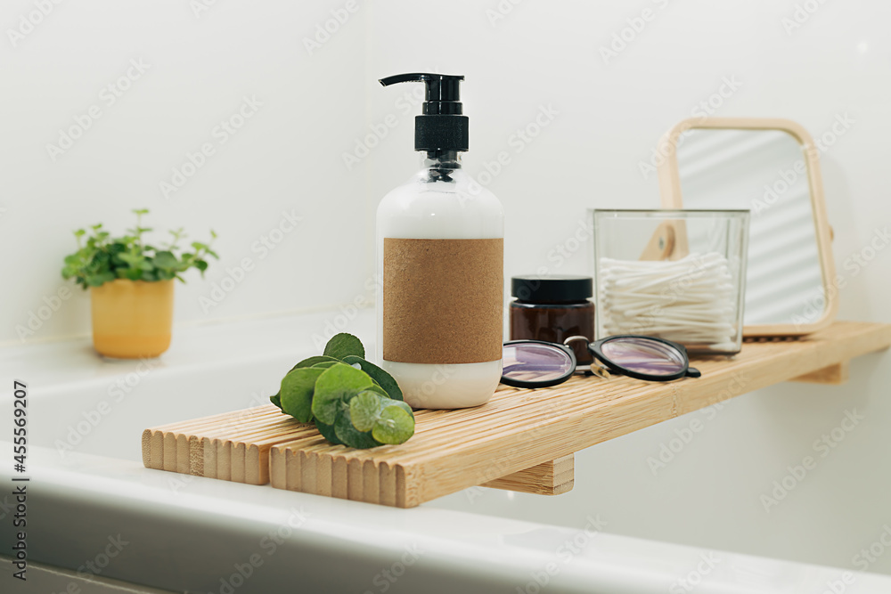 Bathtub wooden tray with beauty cosmetic bottles and accessories in a modern interior scandinavian bathroom with white tiles as a background. Home decor with candles and green plants. Bathtub wooden tray with beauty cosmetic bottles and accessories in a modern interior scandinavian bathroom with white tiles as a background. Home decor with candles and green plants.