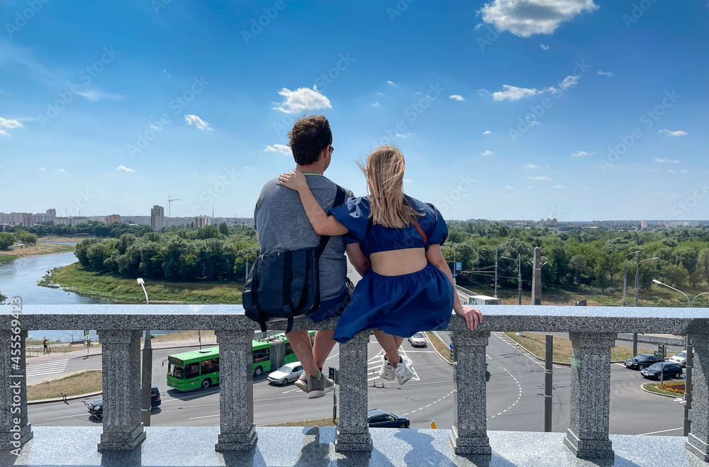 A couple in love sitting on the balcony railing against the blue sky in the big city