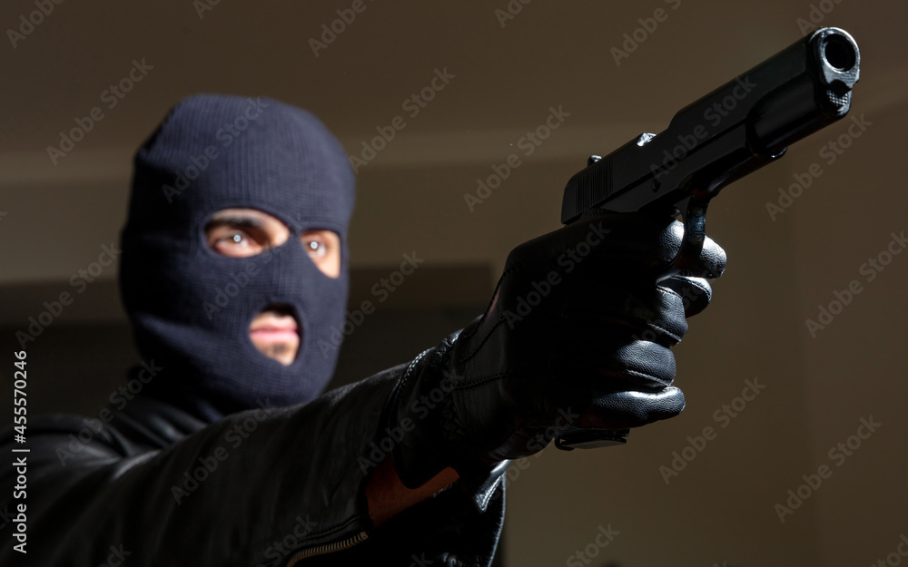 Murderer with balaclava holds gun in leather jacket and gloved hand background. Murderer with balaclava holds gun in leather jacket and gloved hand background.
