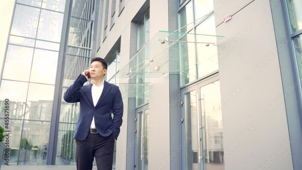 successful young confident businesswoman moving with cellphone in hands against modern office building background downtown Asian business man walks and talks conversation a mobile phone in formal suit successful young confident businesswoman moving with cellphone in hands against modern office building background downtown Asian business man walks and talks conversation a mobile phone in formal suit
