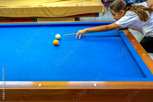 Teenage girl takes aim at a ball sitting on the pool table. Carom billiards or Frecnh billiard photo