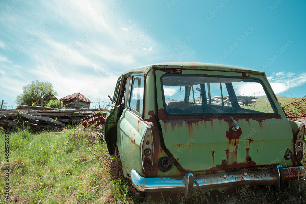 Old rusty car left in a sunny grass village field
