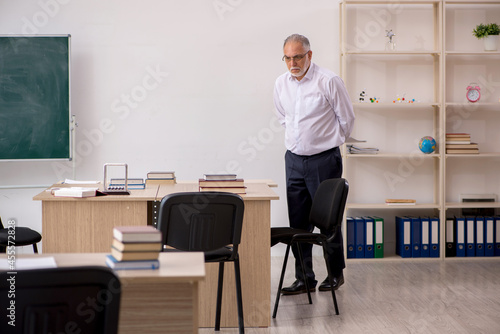 Old male teacher in front of blackboard