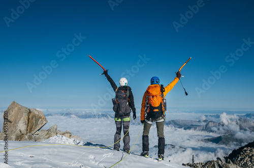 Obraz na plátně Couple dressed mountaineering clothes with backpacks rising arms with ice axes and enjoying views on the summit top near Aiguille du Midi, France