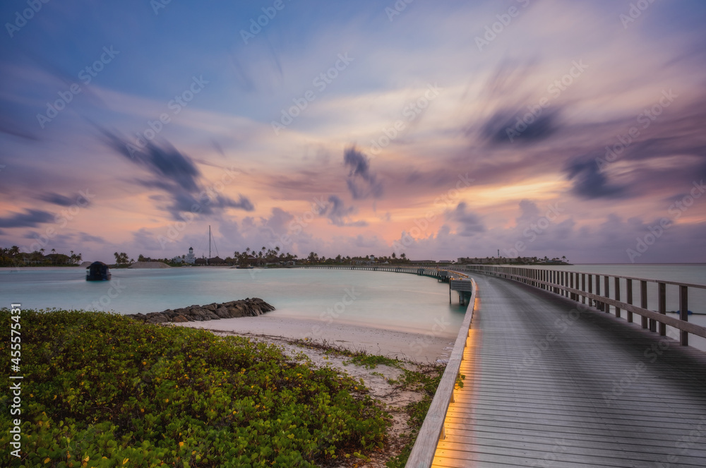 Wooden bridge over the beautiful Maldivian Indian or ocean with sunset sky. Crossroads Maldives, july 2021