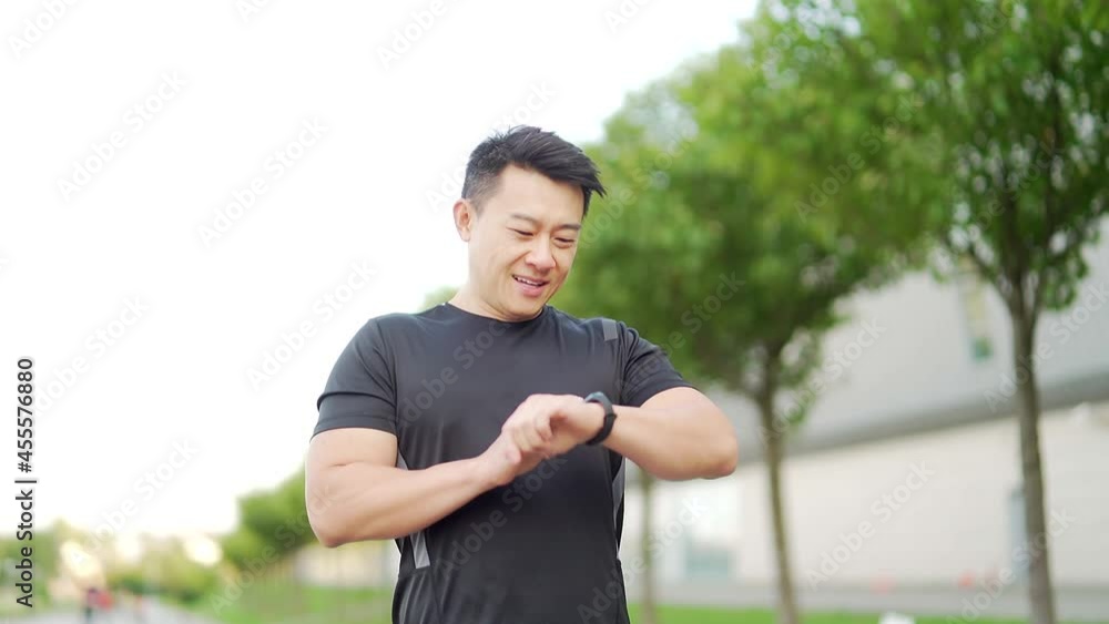 young asian man runner running down the street on urban background of city and park and enjoys fitness watch smart bracelet. Morning jog in black sportswear. Active healthy lifestyle checking tracker young asian man runner running down the street on urban background of city and park and enjoys fitness watch smart bracelet. Morning jog in black sportswear. Active healthy lifestyle checking tracker