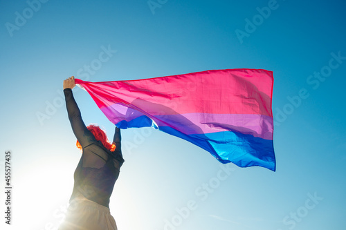 Back view of woman waving colorful flag under blue sky