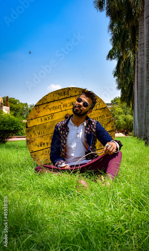 Man in traditional outfit sitting on green grass beside wooden spool photo